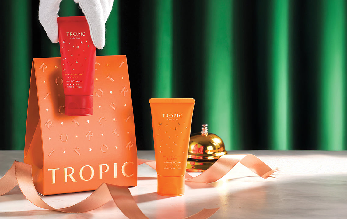 Tropic limited edition Spiced Citrus & Clove body care gift set displayed with festive orange packaging, ribbon, and golden decoration against a green backdrop.